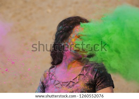 Stunning brunette girl with long wavy hair having fun with green dry Holi powder at the desert