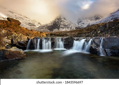 Stunning cascade waterfall at the Fairy Pools on the Isle of Skye in the Scottish Highlands. Taken in the evening golden hour, beautiful light from the sun can be seen in the Winter landscape.	
