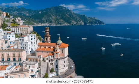 Stunning cliffside villages dot the Amalfi Coast, where vibrant buildings rise above the shimmering blue sea. Sailboats navigate the serene waters on a perfect day under a clear sky. - Powered by Shutterstock