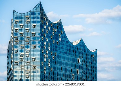 Stunning closeup of the famous glossy glass facade of the iconic Elbphilharmonie concert hall landmark in Hamburg, showcasing its modern, wave-like design and reflecting the sky above in sunlight.