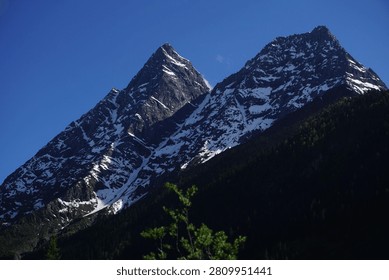 Stunning close-up view of the sharp snow-capped rock peaks of Mount Siguniang under a clear deep blue sky in Sichuan China with dynamic light and shadow.