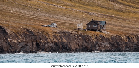 Stunning coastal landscape of Svalbard featuring a rustic cabin by the waterside - Powered by Shutterstock