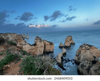 A stunning coastal view with rugged cliffs and rock formations jutting out into the calm blue sea under a partly cloudy sky, showcasing nature's raw beauty and tranquility. - Powered by Shutterstock