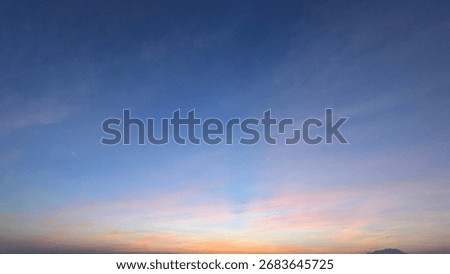 A stunning dawn sky with a dramatic gradient from deep blue to soft pink and gold near the horizon. Long, wispy altocumulus clouds stretch across the entire frame.