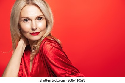 Stunning Elegant Woman, 55 Years Old, Touches Her Healthy Glowing Hair And Looking Sensual At Camera, Wearing Red Dress, Makeup For New Year Party, St Valentines Day, Red Background