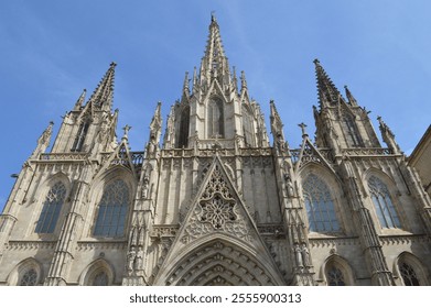 The stunning facade of the Barcelona Cathedral, a prime example of Gothic architecture, showcasing intricate spires, statues, and detailed stone carvings under a clear blue sky - Powered by Shutterstock