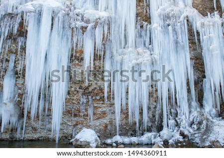 Stunning frozen waterfall icicles  on winter day. Winter cascade frozen into numerous white icicles. Waterfall falling past hundreds of icicles. 