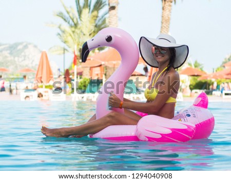 Stunning girl in bikini sits in a pool with blue water on a pink flamingo mattress