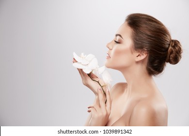 Stunning Girl With Nude Make Up And Naked Shoulders Posing At Grey Background With Flower, Skin Care Concept, Beauty Photo, Close Up Portrait.