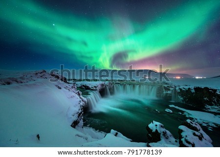 A stunning glowing aurora shape like phoenix bird appears above the landscape of Godafoss waterfall in winter Iceland