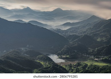 Stunning high angle view of layered mountain peaks fading into heavy morning mist and low clouds over a serene valley lake.