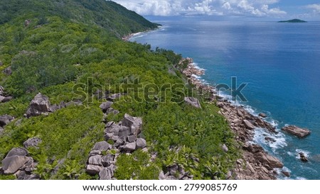 Stunning high-angle drone shot capturing the wild, forested coastline and granite boulders meeting the deep blue ocean waves near Anse Cocos, La Digue, Seychelles.