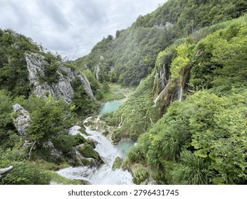 A stunning high-angle panoramic view overlooking cascading waterfalls and crystal-clear turquoise canyon lakes nestled amidst limestone cliffs and lush green forests in Plitvice Lakes National Park, Croatia.