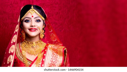 Stunning Indian bride dressed in Hindu red traditional wedding clothes sari embroidered with gold jewelry and a veil smiles tender with extra copy space.