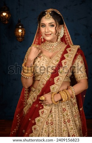 Stunning Indian bride dressed in traditional bridal lehenga with heavy gold jewellery and veil posing fashionable in studio lighting. Wedding fashion and lifestyle.