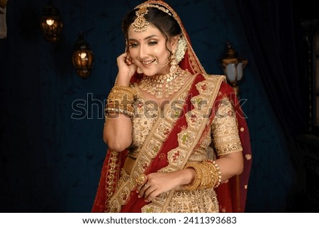 Stunning Indian bride dressed in traditional bridal lehenga with heavy gold jewellery and veil smiles tenderly in studio lighting. Wedding fashion and lifestyle.
