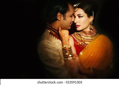 Stunning Indian bride looks at groom with passion while they stand in darkness