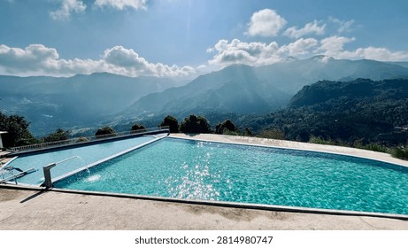 Stunning infinity pool overlooking misty mountain ranges and tropical forest under a bright blue sky with dramatic sunbeams.