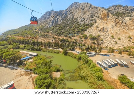 stunning landscape of Antalya, Turkey, a vibrant red cable car glides effortlessly above. Tunektepe mountain peak 605 meters above sea level, unfolds beneath, leading eyes towards a serene green lake.