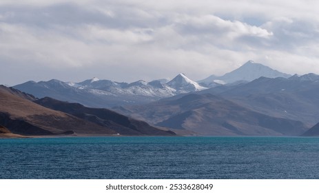 A stunning landscape of a mountain range with snow-capped peaks and a serene blue lake under a partly cloudy sky. - Powered by Shutterstock