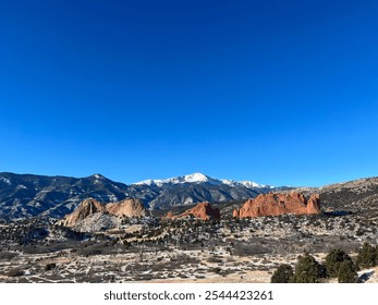 A stunning landscape photograph of Garden of the Gods in Colorado Springs, Colorado, featuring snow-dusted red sandstone rock formations against a backdrop of the majestic snow-capped Pikes Pe - Powered by Shutterstock