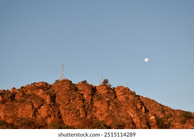 A stunning landscape shot featuring a rocky hill bathed in warm sunset light with a clear sky and a full moon in the distance. Ideal for travel, nature, and outdoor adventure themes and backgrounds.  - Powered by Shutterstock