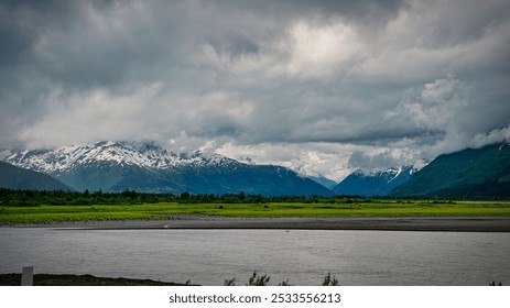 A stunning landscape of snow-capped mountains with a river in the foreground under a cloudy sky. - Powered by Shutterstock