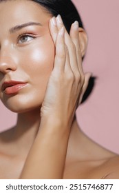 Stunning Latina woman with radiant skin and natural makeup poses with her hand gently touching her face in this close-up portrait against a pink background. Ideal for skincare promotions, beauty