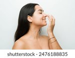 Stunning latina woman in a studio setting touches her nose after a rhinomodelation treatment while looking happy and relaxed