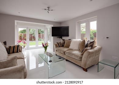 Stunning living room with glass coffee tables, gloss white porcelain tiled floor, white walls, sofas with decorative cushions and bifold patio door leading to garden - Shutterstock ID 2128092917