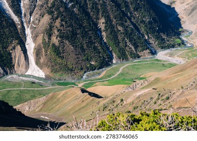 Stunning look-down perspective of a remote alpine valley in Pakistan, captured from a high ridge featuring a prominent snow slide on a forested slope and a meandering stream
