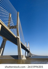 Stunning lowangle view of a modern cablestayed bridge against a vibrant blue sky.