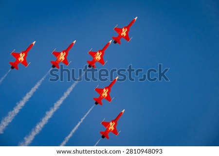 A stunning low-angle view of six red Swiss Air Force F-5E Tiger II fighter jets (Patrouille Suisse) flying in a tight performance formation, leaving t