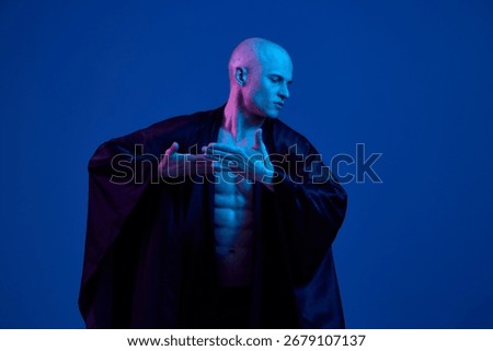 Stunning man in a dramatic pose, showcasing athleticism and grace in a black background with vibrant blue lighting, creating a captivating and stylish atmosphere.