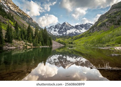 The stunning Maroon Bells mountains rise above a tranquil lake, surrounded by lush greenery and snow-capped peaks under a bright blue sky. - Powered by Shutterstock