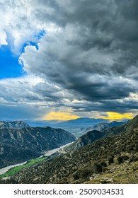 Stunning mountain landscape with dramatic cloud formations and a river cutting through the valley.