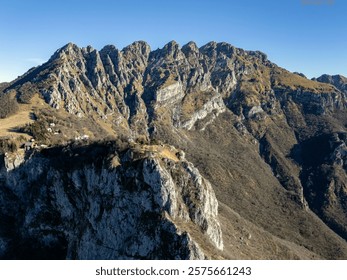 A stunning mountain range under a clear blue sky, showcasing rugged cliffs and sparse vegetation.