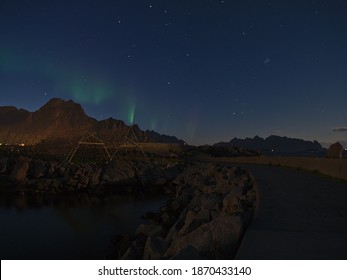 Stunning night view of Svolvær port, Lofoten, Norway with pier, traditional drying racks for stockfish preservation, rugged mountains and clear sky with green colored polar lights (aurora borealis). - Powered by Shutterstock