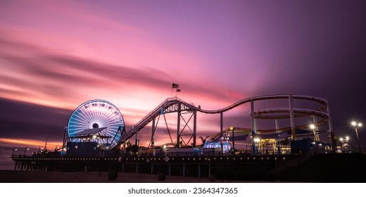 A stunning night-time shot of an amusement park featuring a roller coaster and ferris wheel illuminated in the warm light of a setting sun - Powered by Shutterstock