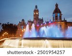 A stunning nighttime shot of an ornate building with colorful lights and a grand fountain in the foreground