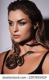Stunning nude woman with python snake elegantly slithering over her neck.