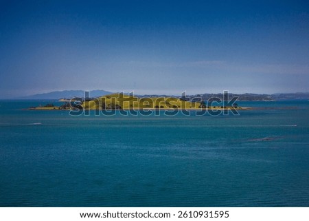 A stunning ocean view featuring a red ferry boat sailing near lush green islands in Auckland, New Zealand. The deep blue water contrasts beautifully with the vibrant landscape under a clear blue sky.