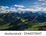 Stunning panorama from the summit of Stanserhorn, showcasing snow-dusted Alpine peaks and lush green valleys below. The clear skies and crisp mountain air add to the breathtaking beauty of this Swiss