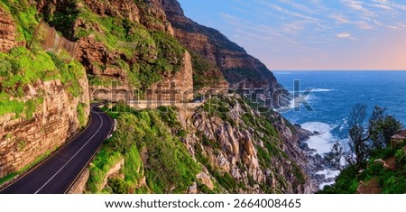 A stunning panoramic view captures the winding Chapman’s Peak Drive along the coastline as the sun sets over the Atlantic Ocean, Cape Town, South Africa
