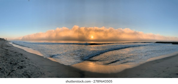 A stunning panoramic view capturing a dense fog bank moving in over the sandy beach and ocean at sunset in Carlsbad, California
