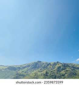 Stunning photograph of a mountainous landscape under a clear blue sky. The photo captures the grandeur of the mountain, which is covered in lush greenery and has a rocky peak. - Powered by Shutterstock