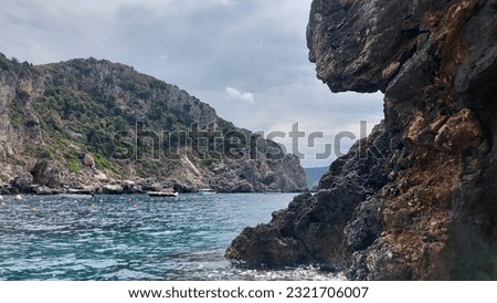 Stunning scenes of natures. Peering around one cliff to another in the near distance. The water is a lovely blue and it is cloudy. there is a boat in the distance