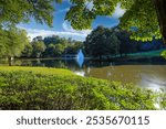 a stunning shot of a lake with a waterfall in the middle of the water surrounded by lush green trees and grass with blue sky and clouds at Lenox Park in Atlanta Georgia USA	