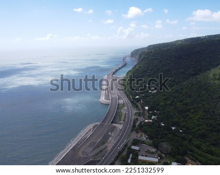 A stunning shot of the new Route du Littoral on La Réunion island. The camera captures the panoramic view of the road, with the beautiful blue ocean on one side and the lush green vegetation on the ot