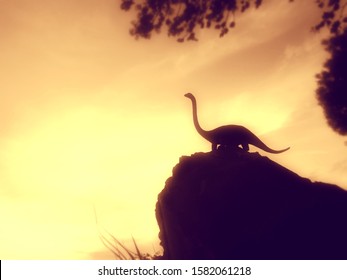 Stunning Silhouette At Sunset Of The Diplodocus Dinosaur, With Its Typical Sauropod Shape, Long Neck And Tail, And Four Sturdy Legs. Jurassic Animal On Top Of The Rocks. Sepia Color Image.